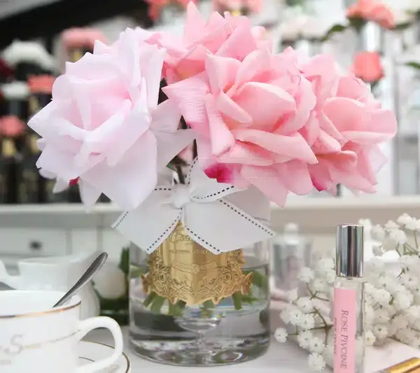 Rosa perfumada e frascos de recarga de perfume de ambiente Côte Noire, junto a chávenas de chá.